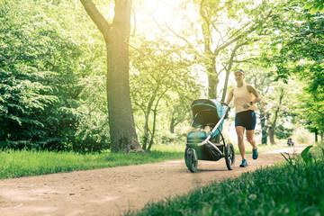 Running woman with baby stroller enjoying summer in park