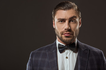 portrait of handsome man in suit and bow tie looking at camera isolated on black