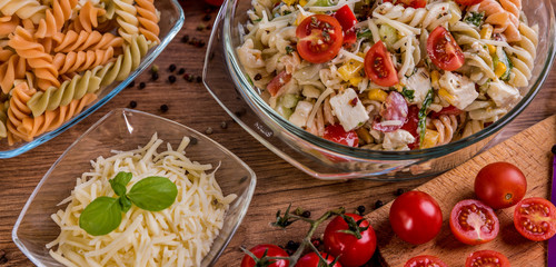 Delicious pasta salad or Mediterranean salad. Tomatoes mozzarella basil corn spice and olive oil on a wooden table. Traditional Italian food