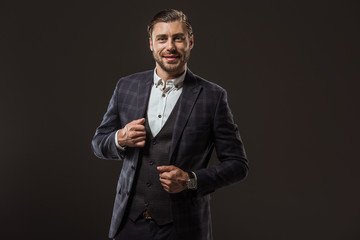 portrait of handsome stylish man in formal wear smiling at camera isolated on black