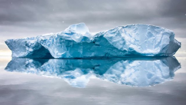 Antarctic Nature. Huge long iceberg floats in open ocean. Dramatic sky, snow fall. Majestic winter landscape. Exploring beauty world, holidays, recreation, travel. 4K Slow motion Parallax Time Lapse