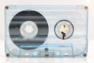 Miniature people: Businessman reading newspaper on tape Cassette. Concept of eduation and business.