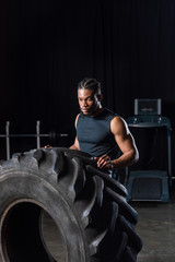 Plakat serious muscular african american sportsman exercising with tyre