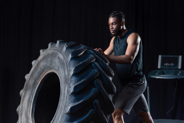 Naklejka na ściany i meble serious african american sportsman training with tire and looking away