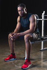 Fototapeta na wymiar full length view of young african american sportsman sitting and looking at camera in gym