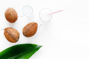 Tropical alcohol-free beverage. Fresh coconut milk in glasses with straw near coconut and palm leaves on white background top view copy space