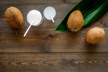 Tropical alcohol-free beverage. Fresh coconut milk in glasses with straw near coconut and palm leaves on dark wooden background top view copy space