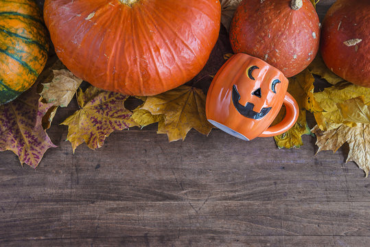 Autumn background: variety of orange pumpkins, halloween face shape mug on dark wooden background with copy space