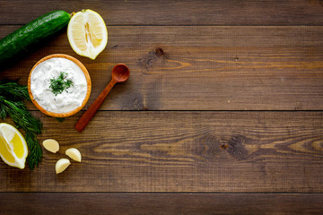 Greek yogurt dip with greenery, cucumber, oranges, garlic on dark wooden background top view space for text