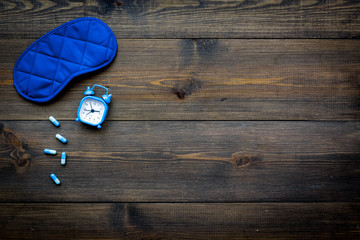 Insomnia concept. Trying to sleep. Help yourself get to sleep. Sleeping pills near sleeping mask and alarm clock on dark wooden background top view copy space