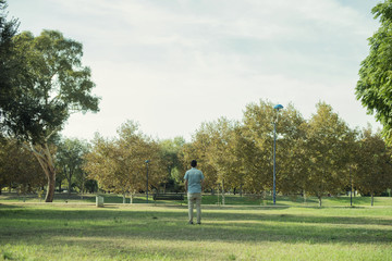 Minimalist portrait of man with his back to the distance in the middle of a landscape of a park or forest with many green trees and a large expanse of grass.