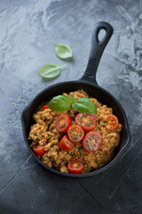 Cuscus with cherry tomatoes, spices and fresh green basil in a cast-iron pan over grey concrete background, vertical shot