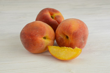 Fototapeta na wymiar Three ripe peaches and half on a white wooden background