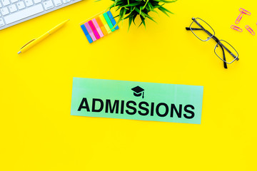 College admission concept. Word admissions with graduation cap sign on yellow student desk with computer top view copy space