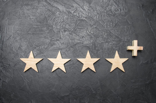 four wooden stars and a plus, on a concrete gray background. The concept of the highest evaluation of quality and service. Better than five stars. Excellent performance and stunning success.