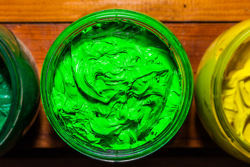 colorful of Plastisol Ink in the clear glass can on the pinewood table for screen print tee shirt. Plastisol ink useful in tee shirt factory and in industry for export.