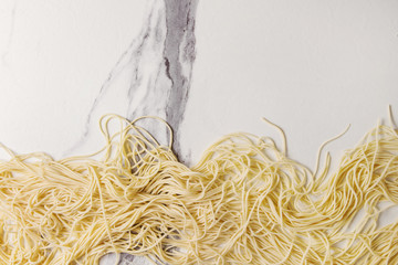 Homemade italian uncooked pasta spaghetti with semolina flour over white marble texture background....