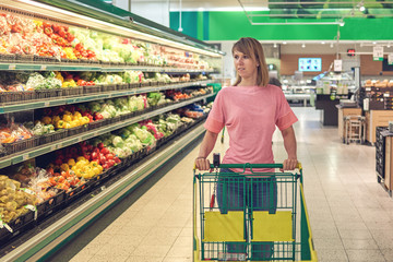 Young Caucasian Woman choosing vegetables during shopping at supermarket.