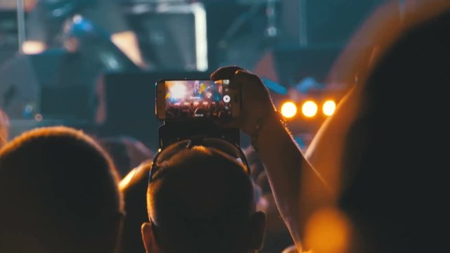 People at Music Rock Concert Taking Photos or Recording Video with Smartphones. Fan person filming on mobile smart phone at concert party crowd cheering at rock music event with flashing light show