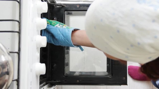 Women opens oven and take off vak belyash - bashkir national homemade meat pies. Bright sunny kitchen.Top view.