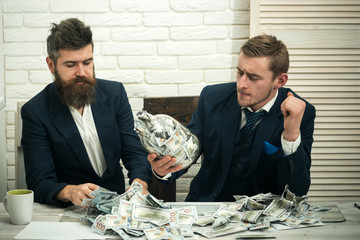 Business partners, businessmen at meeting in office. Cash issues concept. Manager with beard and colleague with jar of cash. Colleagues collecting money in jar instead of bank account