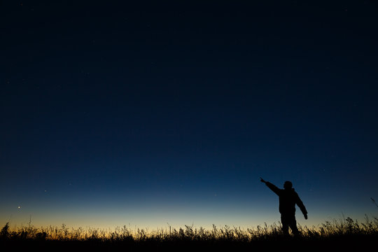 Astronomer points his hand at night the starry sky on a background of a twilight horizon.
