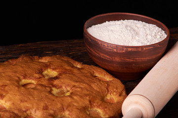 On a dark wooden table, fashionable bakeries, a bowl with flour, apricot cake and tools stand on table