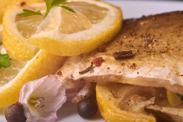 Baked fish with lemon, spices and herbs on white plate on wooden background without head