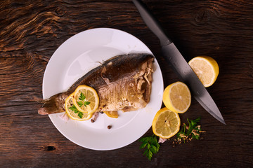 Grilled fish with herbs and lemon on wooden background. Mediterranean luxurious seafood concept