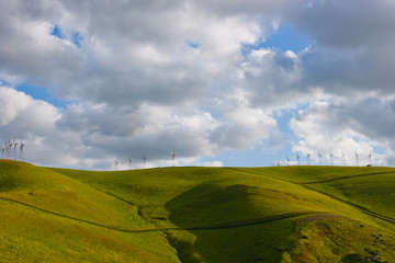 White Cloudy Blue Sky With Green Rolling Hills & Windmills