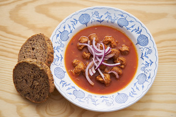 Vegetarian or vegan food or meal made from soya chunks in traditional goulash style with choped red onion served on rustic plate with wholecorn bread as a side dish. 
