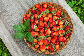 ripe strawberries and mint leaves in a wicker basket on a wooden table