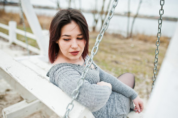 Portrait of brunette girl in gray dress sitting at white wooden construction.