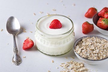 White yogurt in glass bowl with spoon and starwberries on white background.