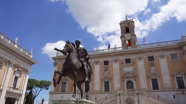Bronze statue of Emperor Marcus Aurelius on horse on Capitol Hill in Rome, Italy in slow motion. Piazza del Campidoglio in summer day. Italian and European Union flags on background