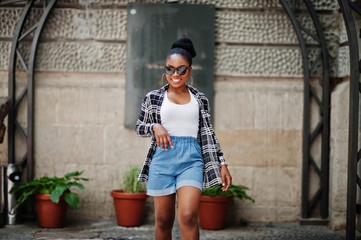 Hip hop african american girl on sunglasses and jeans shorts. Casual street fashion portrait of black woman.