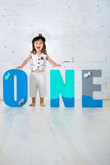 Happy child in a captain's suit with the letters One on a white background of a brick wall