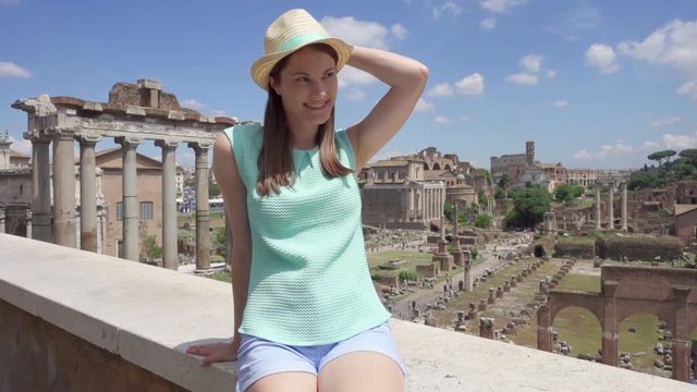 Woman in hat looking at ancient ruins Forum Romanum in slow motion. Happy female tourist enjoying vacation near Roman forum in center of Rome, Italy. Student travel through Europe