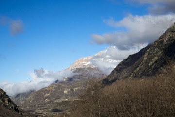 Горный пейзаж. Вершины в белых облаках, Красивый вид на живописное ущелье, панорама с высокими горами. Природа Северного Кавказа, отдых в горах