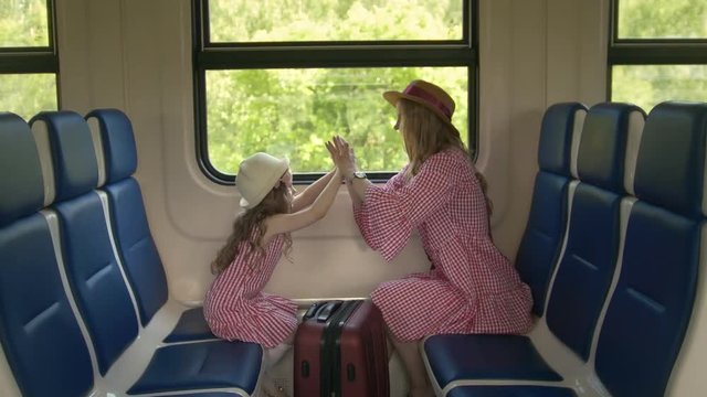 Beautiful mom and cute daughter playing patty-cake sitting in front of window in speed train