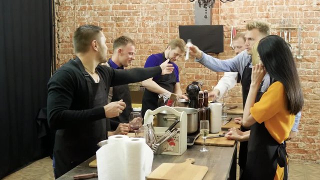 Four young men, three women, one chef cooking a meal at cooking master class. 4K