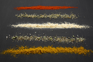 Composition of different spices and herbs over black background, side view.