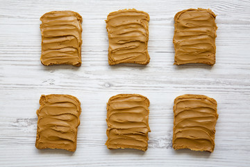 Peanut butter toasts on a white wooden background, top view.