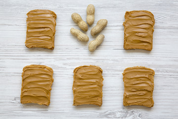 Peanut butter sandwiches and unshelled peanuts on a white wooden background, top view.