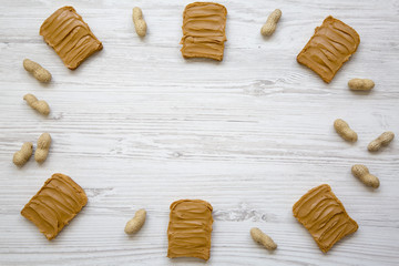 Frame made of peanut butter toasts and unshelled peanuts on a white wooden background, top view. Copy space. From above.