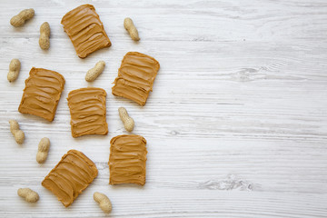 Fototapeta na wymiar Peanut butter toasts and unshelled peanuts on a white wooden background, top view. Copy space. From above.