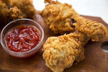 Fried chicken drumsticks with sauce on wooden board, side view. Closeup.