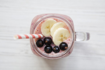 Glass jar with smoothie made of banana, black currant, coconut milk on a white wooden background, top view. Overhead, from above.