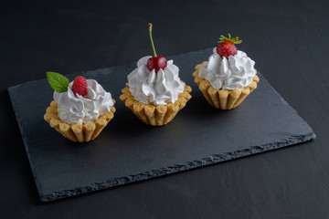 Three cakes with protein cream and berries on dark stone plate on black background