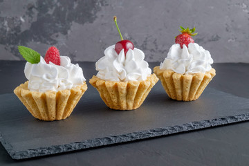 Three cakes with protein cream and berries on dark stone plate on grey background. Close-up view